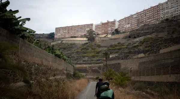 Ciclistas recorren el **barranco de Guiniguada**, con edificios residenciales en la ladera y vegetación seca.