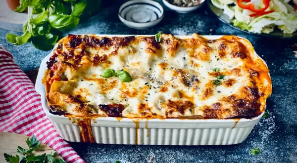 Herzhafte vegetarische Lasagne mit geschmolzenem Käse und frischem Basilikum, serviert in einer weißen Auflaufform.