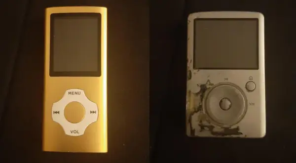 A new gold mp3 player sits next to a worn, scratched silver one.