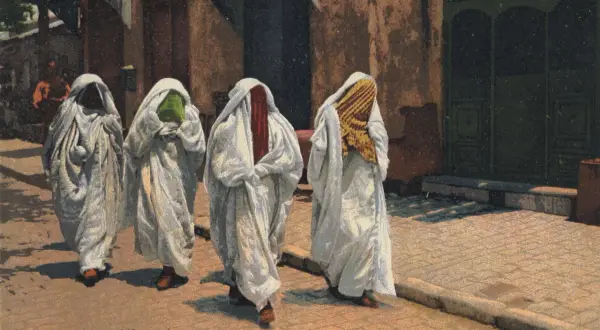 Cztery kobiety w białych, luźnych szatach i welonach, zasłaniających twarze. Czy to burka? Widać fragmenty kolorowych tkanin pod welonami.