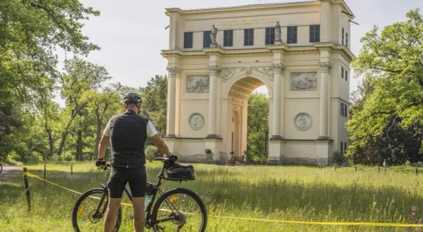 Rowerzysta przed łukiem triumfalnym. Piękne trasy rowerowe Czech zachęcają do odkrywania zabytków.