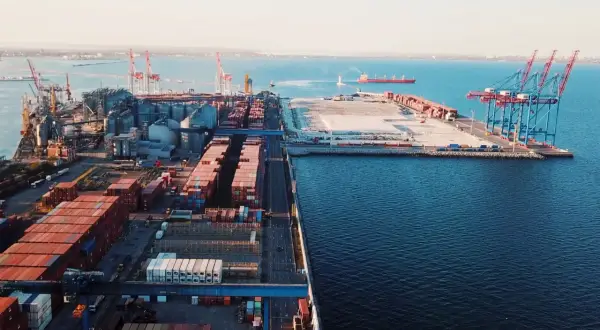 Ogromny port morski z kontenerami i dźwigami, gotowy do eksportu towarów. W oddali widać statek.