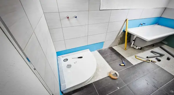 Einbau einer Duschwanne im Badezimmer. Werkzeuge und Rohre liegen bereit.