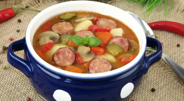 Gęsta zupa węgierska z kiełbasą, ziemniakami, papryką i pieczarkami, udekorowana listkiem bazylii.