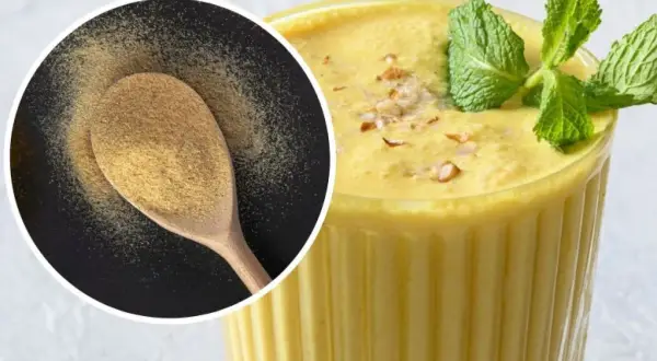 Puszysty mango lassi w szklance, ozdobiony miętą i orzechami. Obok łyżka z proszkiem, być może przyprawą do mango lassi.