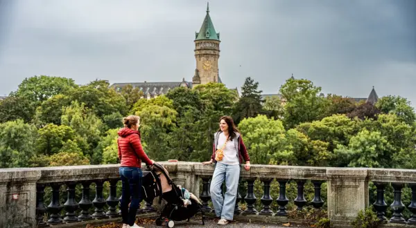 Deux femmes et une poussette devant un bâtiment avec une tour d'horloge, entouré d'arbres.