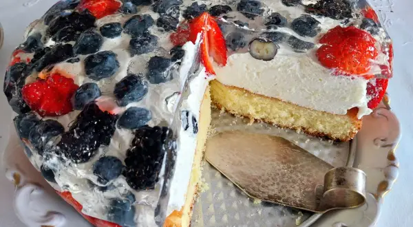 Pyszny biszkopt z kremem i galaretką, ozdobiony świeżymi owocami leśnymi i truskawkami.
