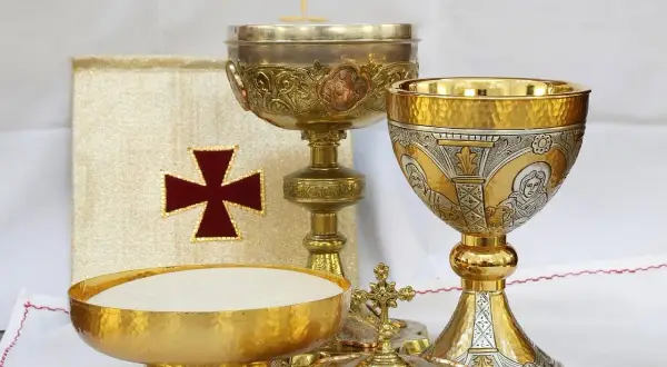 Złoty liturgiczny talerzyk z hostiami, kielichy i księga z krzyżem.