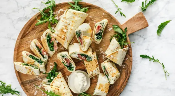 Délicieux wraps coupés en tronçons, garnis de roquette et de jambon, présentés sur un plateau en bois. Une idée simple pour une recette wrap rapide et savoureuse.