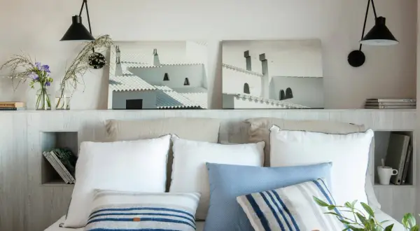 Ideas para hacer un cabecero: dos cuadros de tejados blancos, lámparas negras y cojines a rayas sobre una cama.