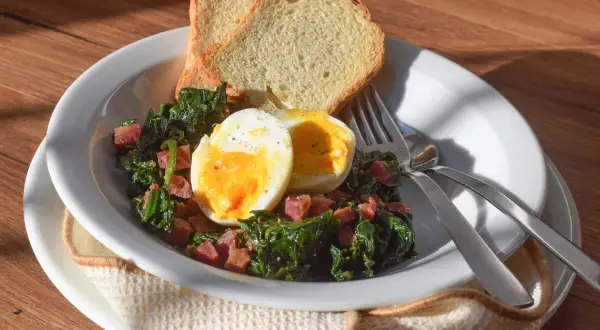Plato de espinacas con jamón, huevo duro y tostadas. Un desayuno o almuerzo saludable y delicioso.