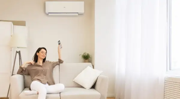Donna rilassata sul divano, telecomando in mano, con il condizionatore acceso per una perfetta traduzione del comfort.