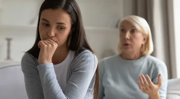 En ung kvinna sitter med handen mot munnen, ser bekymrad ut. Bakom henne gestikulerar en äldre kvinna, kanske en diskussion om ett problem med vuxen dotter.