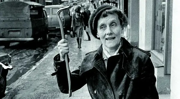 Kobieta z łomem na ulicy, uśmiecha się, jakby mówiła "życie ci niemiłe". W tle samochody i przechodnie.