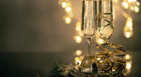 Deux flûtes de champagne pétillant, décorées de rubans dorés, prêtes pour organiser une soirée de nouvel an. Lumières festives en arrière-plan.