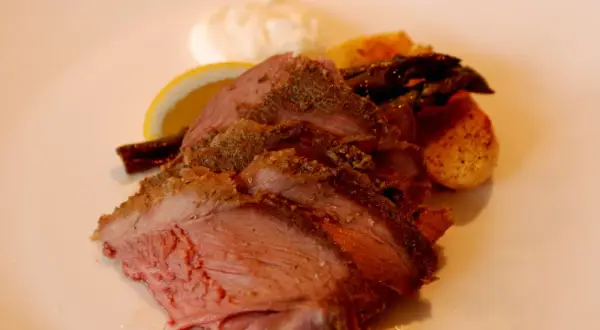 Skivad lammstek med ben, serverad med rostade potatisar, sparris, citronklyfta och en klick sås.