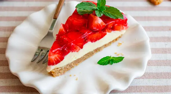 Ein Stück Erdbeer-no-bake-cheesecake mit frischer Minze auf einem weißen Teller, daneben eine Gabel.