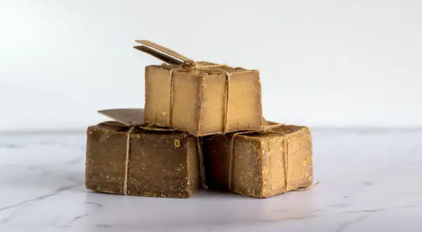 Tres cubos de jabón natural, atados con cuerda rústica, apilados sobre una superficie de mármol.