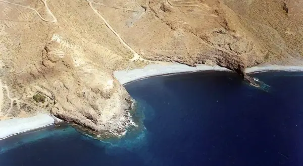 Vista aérea de la playa del medio, una cala rocosa con aguas azules profundas y senderos en las laderas áridas.