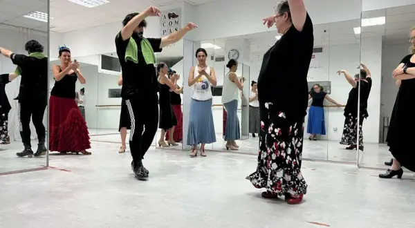 Clase de flamenco facil. Varias personas practican pasos de baile frente a espejos, con movimientos elegantes y faldas amplias.