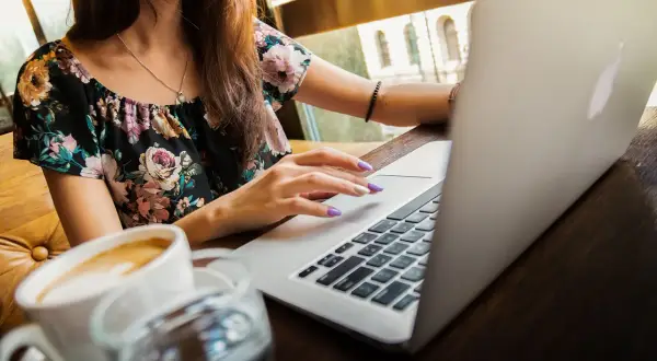 Kobieta z fioletowymi paznokciami pracuje na MacBooku, obok kawa. Nagrywanie ekranu macbooka w kawiarni.