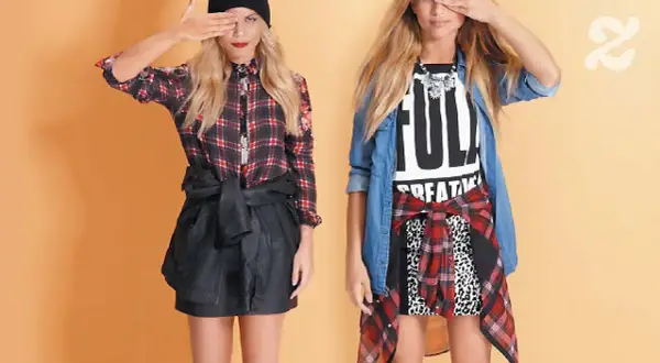 Deux jeunes femmes adoptent un style grunge avec des chemises à carreaux, des jupes en cuir et des t-shirts graphiques.