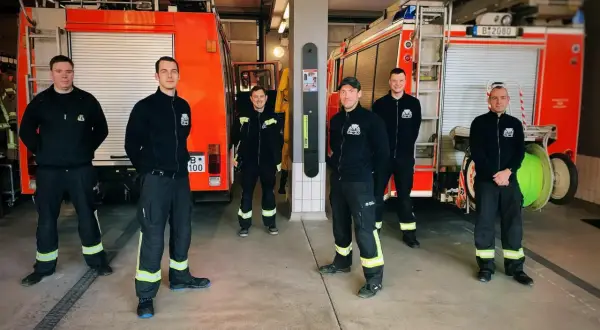 Sechs Männer in Einsatzkleidung stehen vor zwei Feuerwehrautos. Sie leisten ehrenamtlich Dienst bei der Feuerwehr und sind bereit für den nächsten Einsatz.