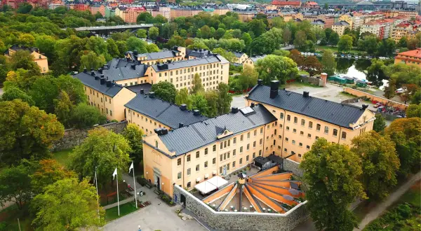 Långholmen vandrarhem, en före detta fängelsebyggnad i Stockholm, omgiven av grönskande träd och med en vacker utsikt över vattnet.