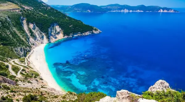 Widok na Myrtos, jedną z najpiękniejszych plaż i głównych **kefalonia atrakcje**. Biały piasek, turkusowa woda i strome klify.