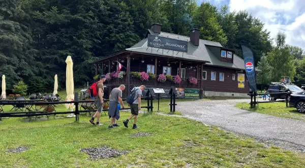 Drewniany budynek schroniska "U Góralki" w Bieszczadach, z trzema mężczyznami idącymi po trawie.