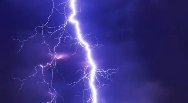 Potężne wyładowanie, przepięcie prądu rozświetla nocne niebo. Błyskawice rozchodzą się niczym gałęzie drzewa.