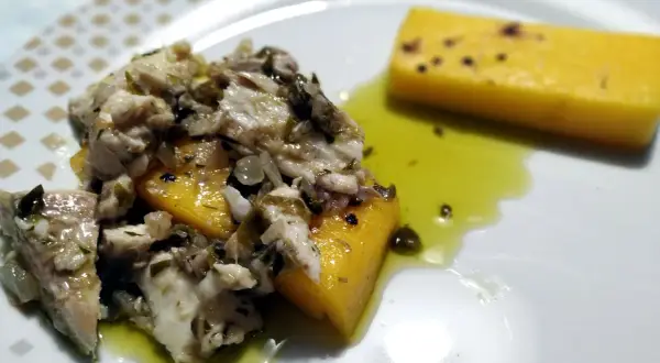 Piatto di luccio in umido con polenta gialla, condito con erbe aromatiche e olio. Un sapore autentico da provare!