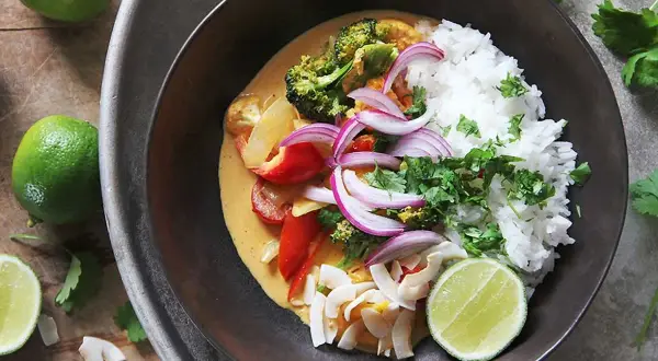 En skål med klimatsmart mat: ris, broccoli, paprika, rödlök och kokosflingor i en krämig currysås, toppad med lime och koriander.