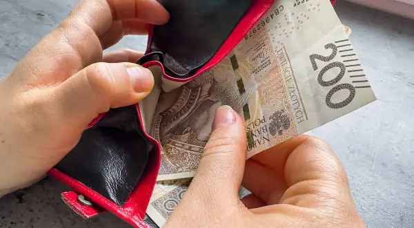 Dwie ręce wkładają banknot 200 zł do czerwonego portfela. Czy kosiniakowe wlicza się do dochodu?