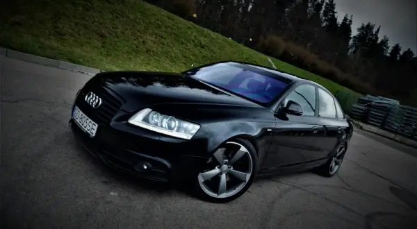 Czarny Audi A6 C6 3.0 TDI Quattro S-line na tle zielonego wzgórza i lasu.
