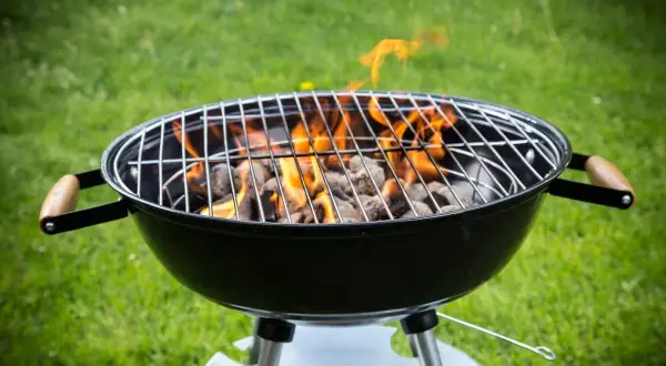 Rozpalony grill węglowy z płomieniami na trawie. Idealny do nauki, jak rozpalic grilla na letnie wieczory.