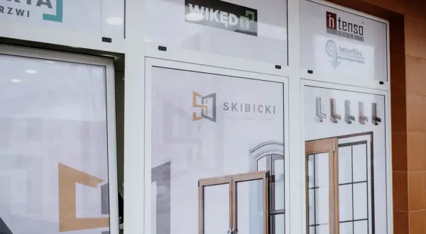 Witryna sklepowa z logo firm okiennych i drzwiowych oraz zdjęciami produktów.