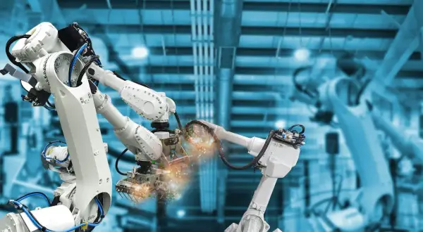 Różne rodzaje robotów przemysłowych pracują w fabryce, spawając elementy z iskrami.