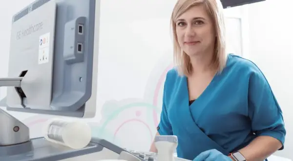 Lekarka w niebieskim fartuchu przy aparacie USG. Czy ginekolog jest na NFZ? Zapytaj w swojej przychodni.