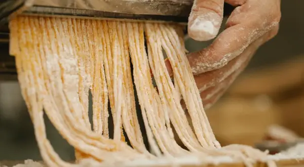 Färska pastastrådar skärs från en pastamaskin, en påminnelse om vart kommer pasta ifrån.
