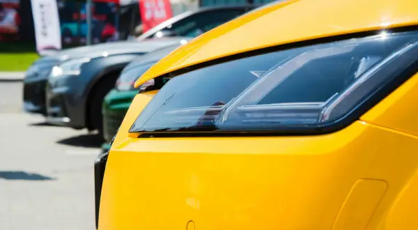 Gros plan sur le phare d'une voiture jaune vif, avec d'autres voitures en arrière-plan. Pensez à la résiliation de votre assurance auto pour ce bolide.