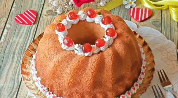 Delicioso bizcocho con forma de anillo, decorado con crema, cerezas y corazones. Un dulce baba al ron perfecto para celebrar.
