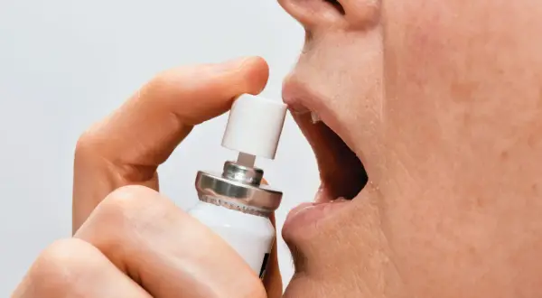 En person använder nitroglycerin spray under tungan för snabb lindring.