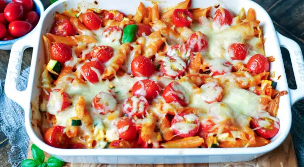 Ein köstlicher nudelauflauf vegetarisch mit Penne, Kirschtomaten und geschmolzenem Käse, garniert mit frischem Basilikum.