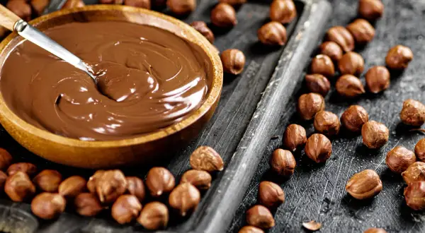 Schokocreme selber machen: Eine Schüssel voller cremiger Schokocreme neben gerösteten Haselnüssen auf einem Holzbrett.