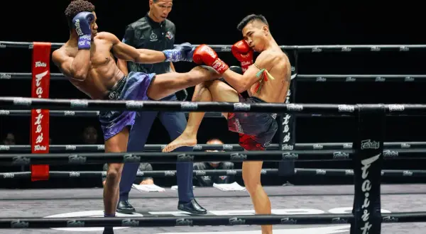 Två thaiboxare i full action i Lumpinee Stadium. En spark möter ett block.