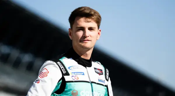 Logan Sargeant, piloto de carreras, posa con su traje de competición blanco y turquesa, listo para la acción.
