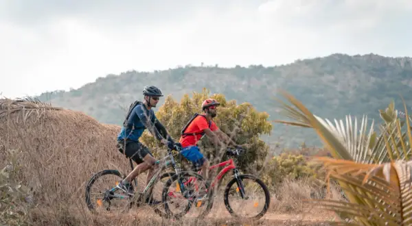 Dos ciclistas disfrutan de rutas en bici para principiantes en un paisaje rural con colinas y vegetación seca.