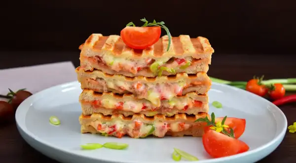 Gestapelte Sandwiches mit geschmolzenem Käse und Gemüse, perfekt für kontaktgrill rezepte. Garniert mit Tomaten und Frühlingszwiebeln.