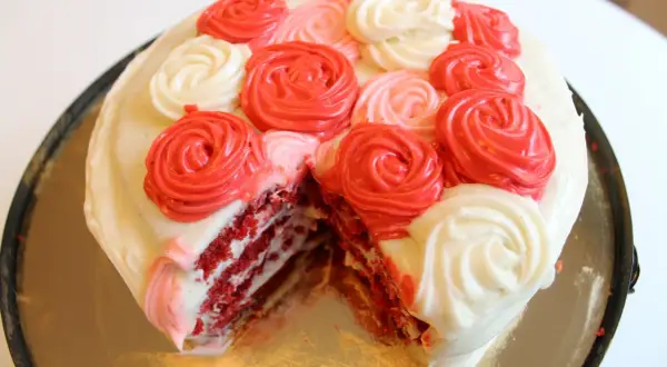 En skivad red velvet cake med vit frosting och dekorationer i form av röda och rosa rosor.